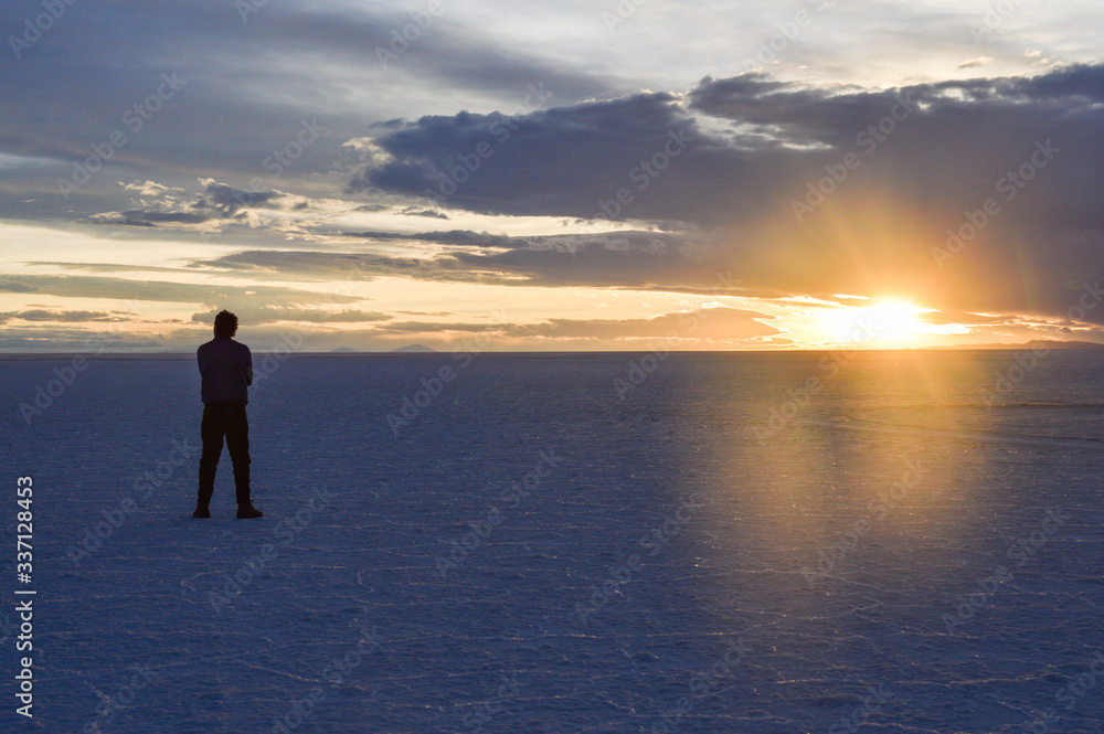Man in the Uyuni desert standing with arms crossed and looking to the side at the time of sunset