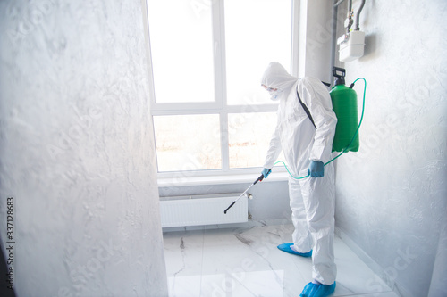 Coronavirus Pandemic. A disinfector in a protective suit and mask sprays disinfectants in house. Protection against COVID-19 disease. Prevention of spreding pneumonia virus with surfaces. photo