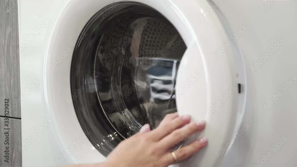 Female hand with married ring takes GREEN SNEAKERS from laundry machine. Loading washing machine. Load clothes to washer machine. Load clothes laundry washing machine. Preparing laundry washing Female hand with married ring takes GREEN SNEAKERS from laundry machine. Loading washing machine. Load clothes to washer machine. Load clothes laundry washing machine. Preparing laundry washing