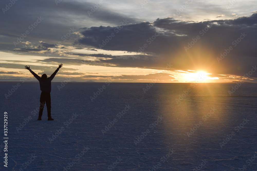 Man in in the Uyuni desert with arms up at the time of sunset