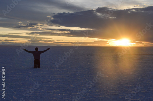 Silhouette of man kneeling in the Uyuni desert with open arms at the time of sunset
