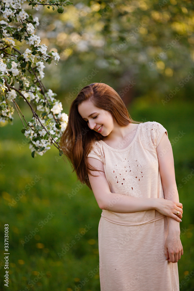 Young woman in beige dress in a blooming apple garden. Spring story. Brown-haired romantic girl with long hairs. Woman plays with her hairs. Woman portrait. Walk in a spring park Young woman in beige dress in a blooming apple garden. Spring story. Brown-haired romantic girl with long hairs. Woman plays with her hairs. Woman portrait. Walk in a spring park