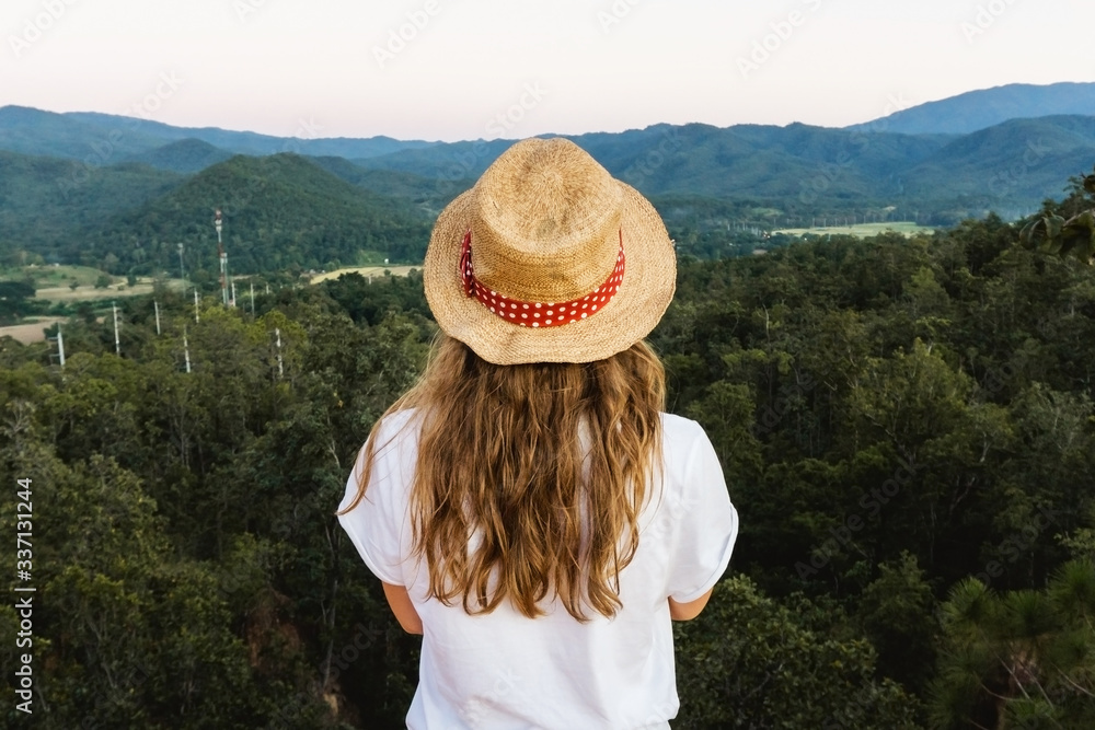 Fototapeta premium Girl standing on the edge of the cliff watching the panorama. Top view forest landscape. Travel lifestyle background. Straw hat fashion. Woman enjoy the view after trekking up the mountain in Thailand