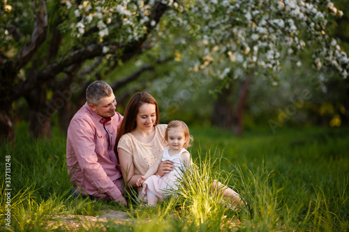 little daughter with parents on a picnic in blooming apple garden. Mom loves her child. Spring story. Toddler girl with family in apple garden. Happy family in beautiful spring day. Tender relations