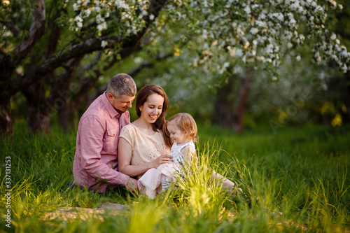 little daughter with parents on a picnic in blooming apple garden. Mom loves her child. Spring story. Toddler girl with family in apple garden. Happy family in beautiful spring day. Tender relations © Olga Mishyna