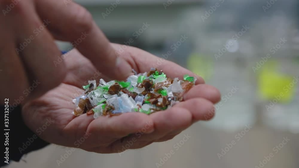 a man touches colored parts from chopped plastic bottles on the palm of his hand a man touches colored parts from chopped plastic bottles on the palm of his hand