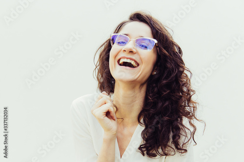 Happy stylish woman in glasses laughing at camera with open mouth. Wavy haired young woman in casual shirt standing isolated over white background. Positive emotion or joy concept