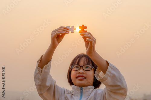 Little child holding piece of blank jigsaw puzzle at sunset background