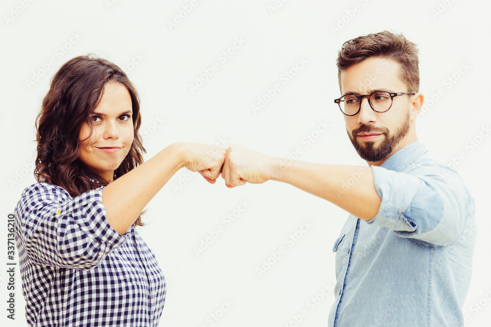 Proud couple making fist bump gesture. Young woman in casual and man in glasses standing isolated over white background. Teamwork concept Proud couple making fist bump gesture. Young woman in casual and man in glasses standing isolated over white background. Teamwork concept