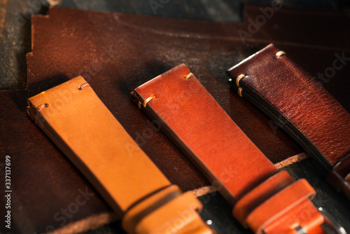 Handmade brown tone watch straps with steel buckle laying on wooden rustic surface next to leather cuttings and leather thread. Different leather colour tones.