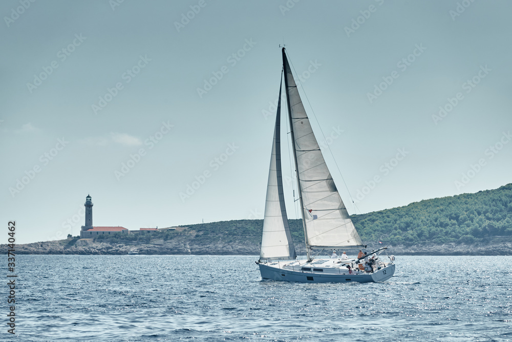 Seascape of the sailboat in the foreground, the lighthouse on the island is on background, Croatia, at sunset, a rocky coast, ladder to a beacon, a small cape Seascape of the sailboat in the foreground, the lighthouse on the island is on background, Croatia, at sunset, a rocky coast, ladder to a beacon, a small cape