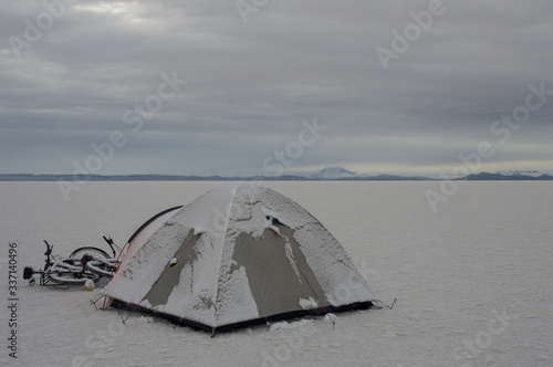 isolated tent and snow-covered bikes in the salt desert in Bolivia © Nataly Regina