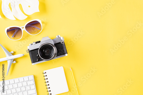 Retro film camera, sunglasses, note book, airplane, keyboard and hat on yellow pastel background for travel summer holiday and vacation concept.