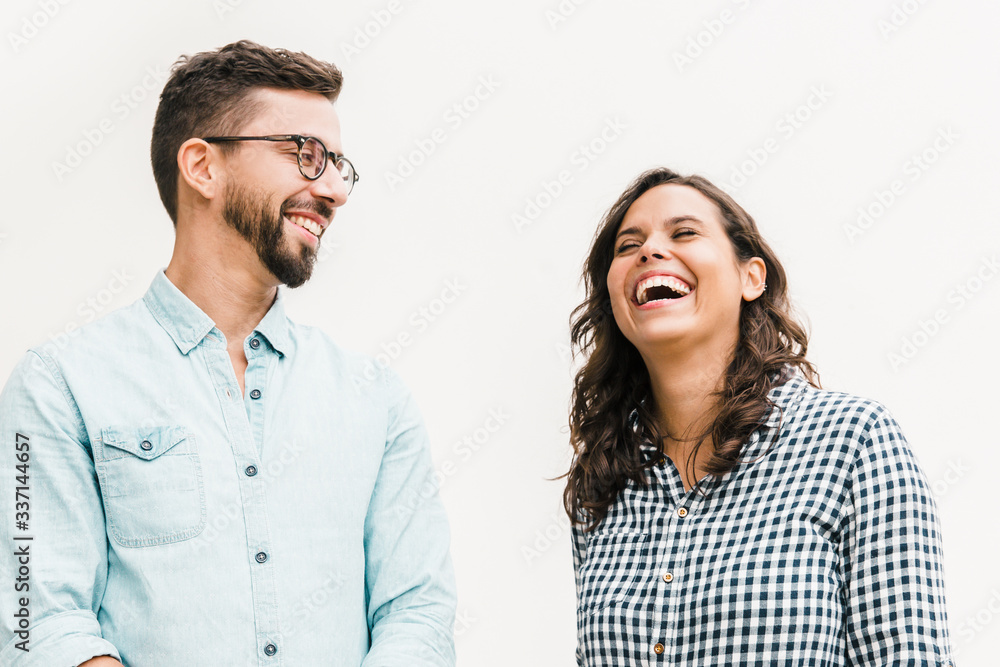Positive funny guy making his girlfriend laugh. Young woman in casual and man in glasses in glasses posing isolated over white background. Having fun together concept Positive funny guy making his girlfriend laugh. Young woman in casual and man in glasses in glasses posing isolated over white background. Having fun together concept