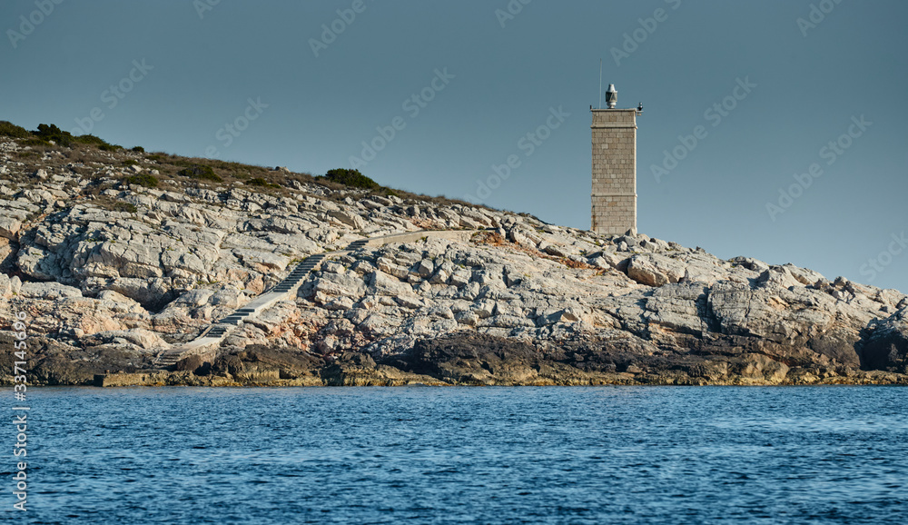 The lighthouse on the island in Croatia nearby Vis at sunset, a rocky coast, ladder to a beacon, a small cape