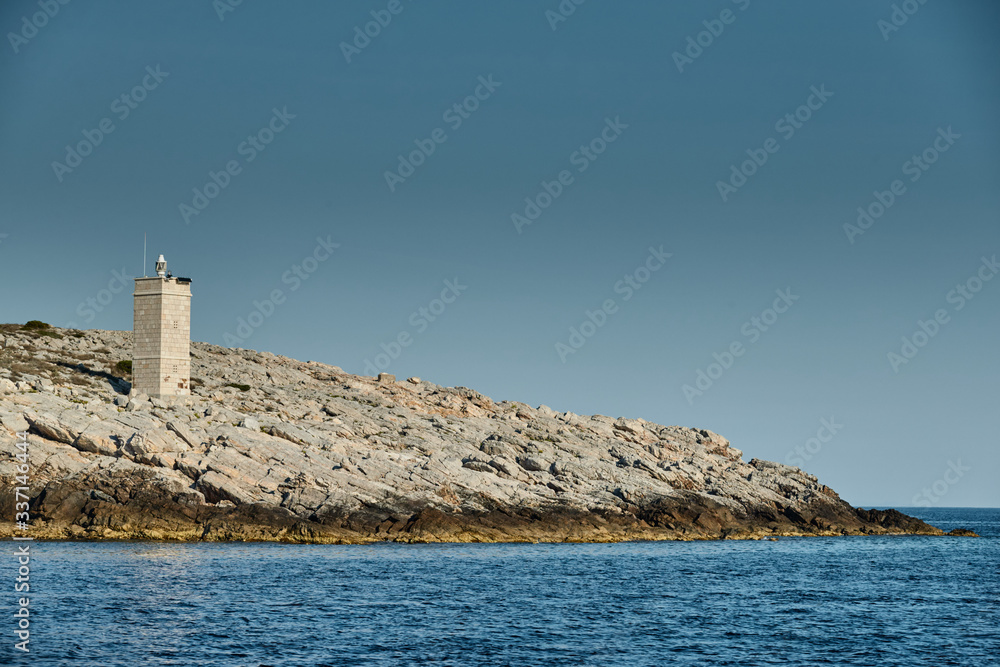 The lighthouse on the island in Croatia nearby Vis at sunset, a rocky coast, ladder to a beacon, a small cape