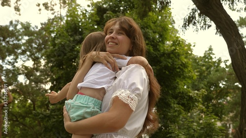 mom hugs happy child. Beautiful mother and her baby are playing in park. Happy Mother's Day Joy. Mom and baby 4K. happy childhood concept. happy mom hugs little daughter in the park outdoors.
