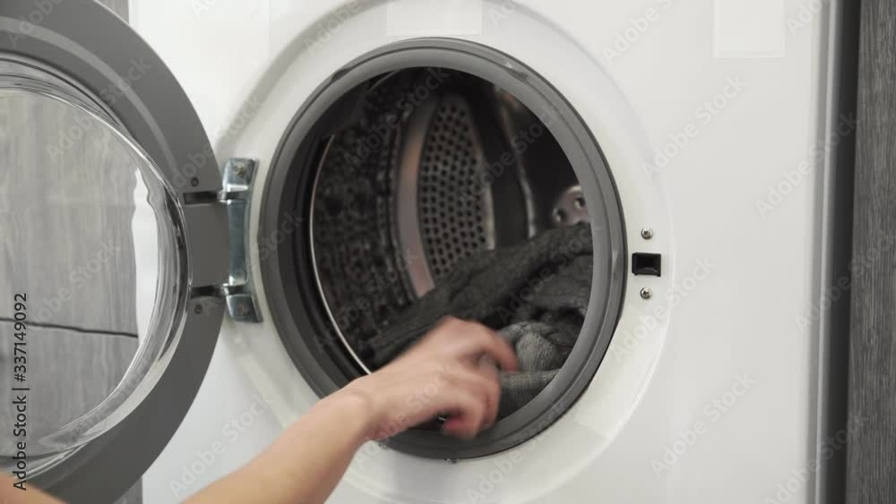 Female hand puts GREY SWEATER in laundry machine. Loading washing machine. Load clothes to washer machine. Load clothes laundry washing machine. Preparing laundry washing Female hand puts GREY SWEATER in laundry machine. Loading washing machine. Load clothes to washer machine. Load clothes laundry washing machine. Preparing laundry washing