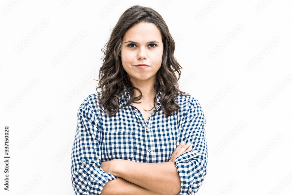 Positive determined student girl with arms crossed and funny grimace looking at camera. Young woman in casual checked shirt standing isolated over white background. Human emotion concept