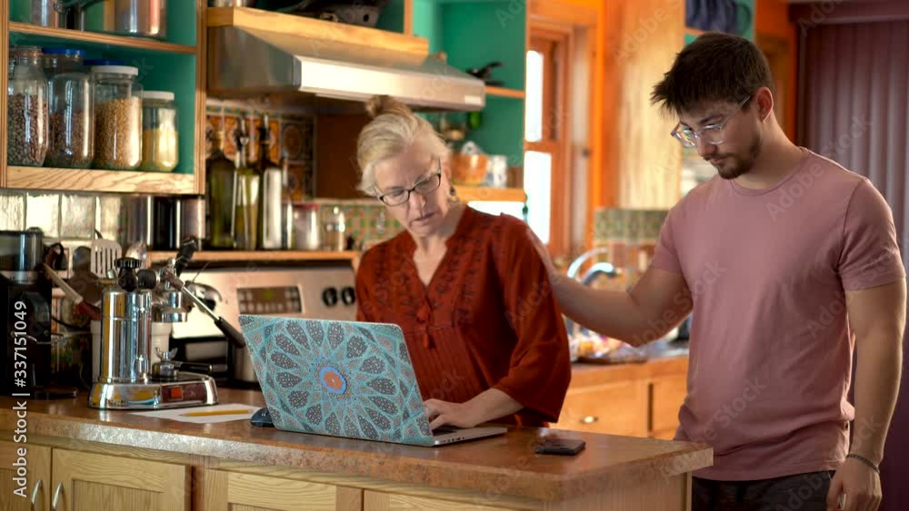 Teen son acts as tech support and pushes his mother out of the way so he can use her computer in a kitchen. Teen son acts as tech support and pushes his mother out of the way so he can use her computer in a kitchen.