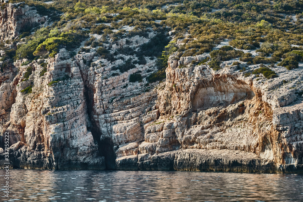 Beautiful high cliff with caves and hanging rocks of a mountain in Adriatic sea, a crevice, colorful