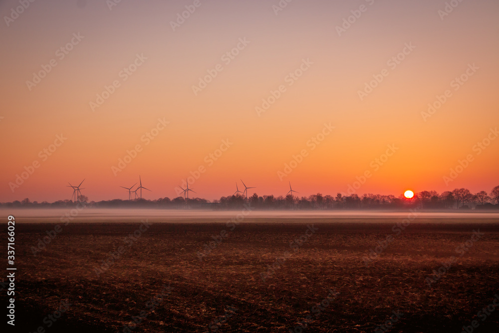 Beautiful sunrise in the Netherlands with a wide view over the misty fields and a beautiful orange rising sun in the background Beautiful sunrise in the Netherlands with a wide view over the misty fields and a beautiful orange rising sun in the background