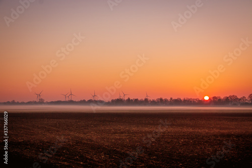 Beautiful sunrise in the Netherlands with a wide view over the misty fields and a beautiful orange rising sun in the background
