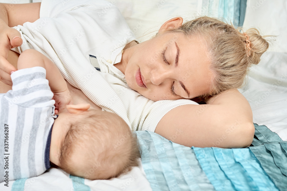 Young mother breastfeeds her baby, lying on bed and touching him hands.  Mothers day concept. Maternity and healthy lifestyle. Lactation infant concept.