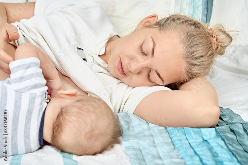 Young mother breastfeeds her baby, lying on bed and touching him hands. Mothers day concept. Maternity and healthy lifestyle. Lactation infant concept.