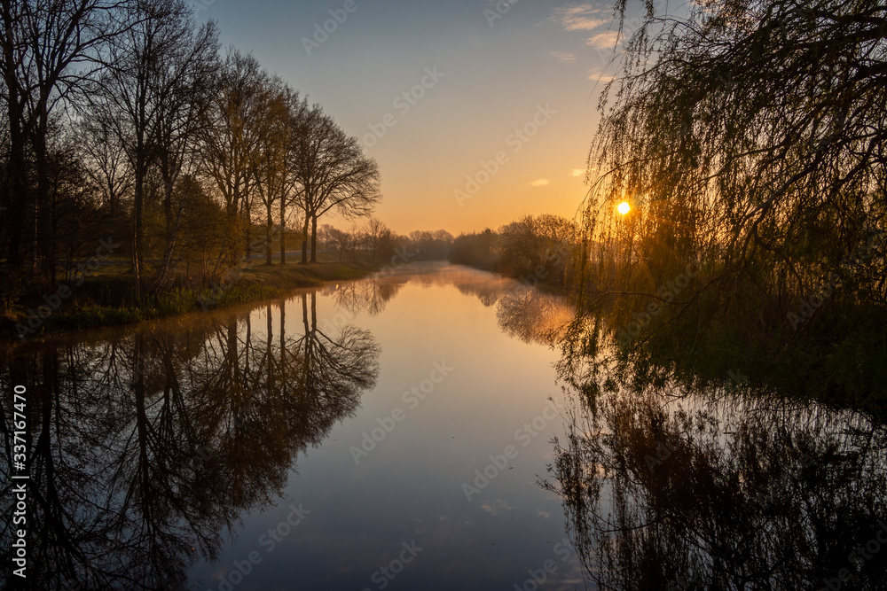 Atmospheric sunrise in the Netherlands with a beautiful orange glow in the air and water vapor over the fields and the canal and ponds Atmospheric sunrise in the Netherlands with a beautiful orange glow in the air and water vapor over the fields and the canal and ponds