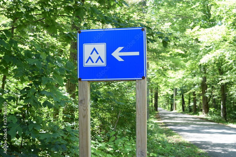 Blue tent site sign in a camping, with hiking trail in the back. Campground directions. Blue tent site sign in a camping, with hiking trail in the back. Campground directions.