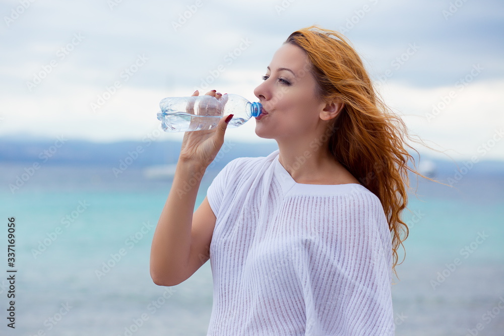 Naklejka premium beautiful young woman drinking water in summer beach outdoor with sea background