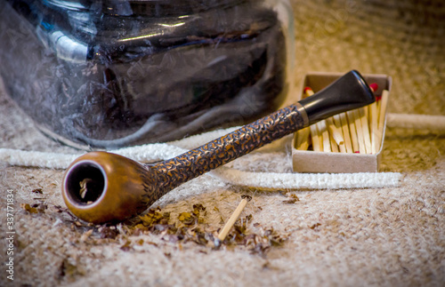 Carved artisan pipe on a rustic background has tobacco,  pipe tools, cleaners and match sticks ready for a good smoke photo