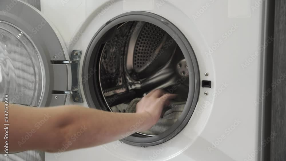 Female hand puts GREY PANTS in laundry machine. Loading washing machine. Load clothes to washer machine. Load clothes laundry washing machine. Preparing laundry washing Female hand puts GREY PANTS in laundry machine. Loading washing machine. Load clothes to washer machine. Load clothes laundry washing machine. Preparing laundry washing