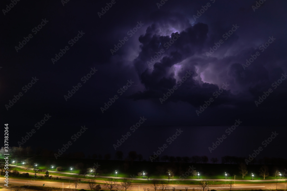 An intense thunderstorm cloud with blue or purple colors and lit up with numerous lightning strikes moves over Lake Michigan as cars pass by on Lake Shore Drive on Chicago's north side.