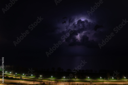 An intense thunderstorm cloud with blue or purple colors and lit up with numerous lightning strikes moves over Lake Michigan as cars pass by on Lake Shore Drive on Chicago's north side.