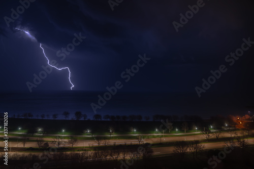A bright bolt of lightning shoots out of a thunderstorm cloud as the storm moves over Lake Michigan and cars pass by on Lake Shore Drive on Chicago's north side at night.