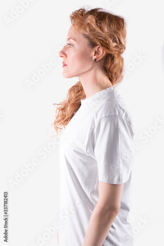 Woman with curly hair in casual t-shirt stands sideways, looks straight ahead