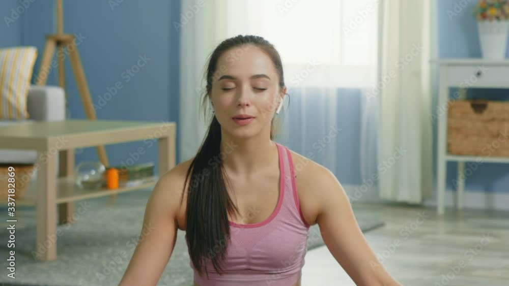 Young woman practices relaxing breathing, sitting on a floor at home, trying to relieve stress, listening music, keeping eyes closed, slow motion. Young woman practices relaxing breathing, sitting on a floor at home, trying to relieve stress, listening music, keeping eyes closed, slow motion.