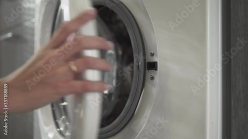 Female hand with married ring takes WHITE CLOTHES from laundry machine. Loading washing machine. Load clothes to washer machine. Load clothes laundry washing machine. Preparing laundry washing
