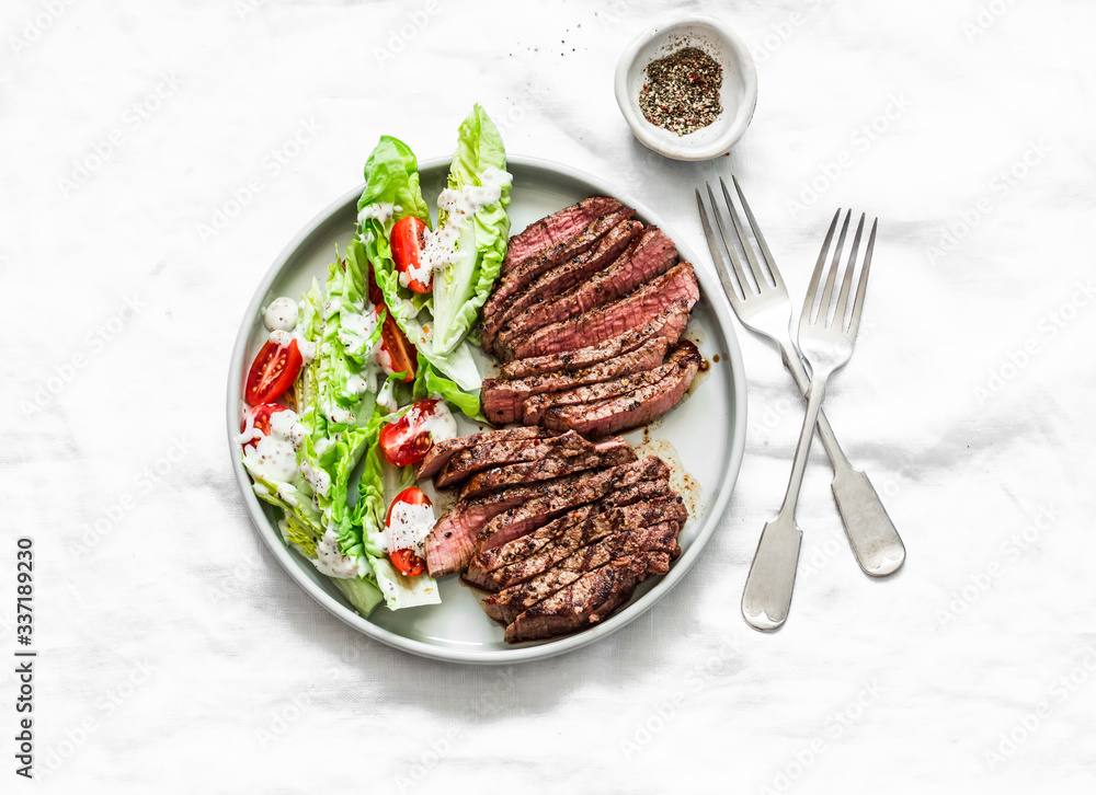 Medium rare beef steak and romaine cherry tomatoes yogurt dressing salad on a light background, top view.Delicious balanced food Medium rare beef steak and romaine cherry tomatoes yogurt dressing salad on a light background, top view.Delicious balanced food