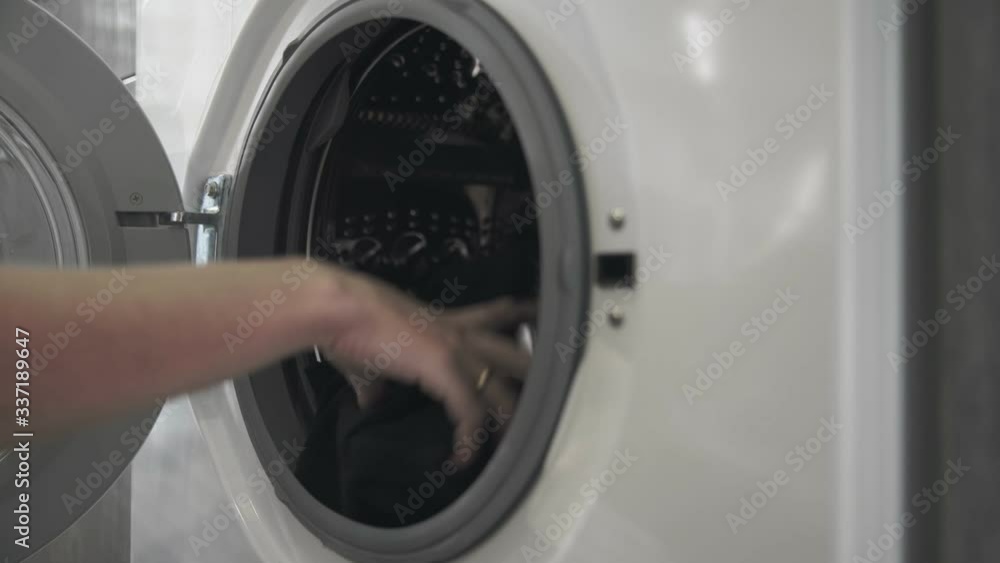 Female hand with married ring puts BLACK CLOTHES in laundry machine. Loading washing machine. Load clothes to washer machine. Load clothes laundry washing machine. Preparing laundry washing Female hand with married ring puts BLACK CLOTHES in laundry machine. Loading washing machine. Load clothes to washer machine. Load clothes laundry washing machine. Preparing laundry washing