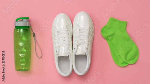 White sneakers, green socks and a green sports bottle on a red background. A set of sports accessories.