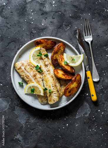 Tablou canvas Fish fillet baked with lemon and new potatoes on a dark background, top view