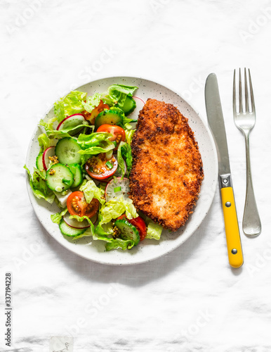 Chicken milanese and fresh romaine salad, cherry tomatoes, radishes, cucumbers salad - delicious lunch on a light background, top view