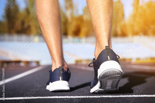 Sporty man running at stadium on sunny morning, closeup