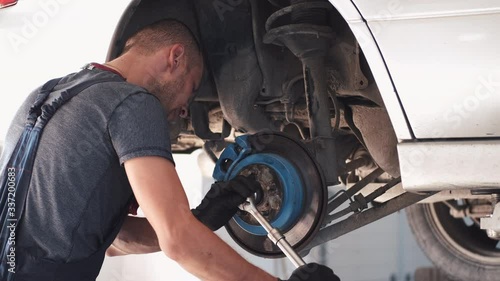 Man repairs white car. Machine is without wheels. Worker is fixing car in service center. photo