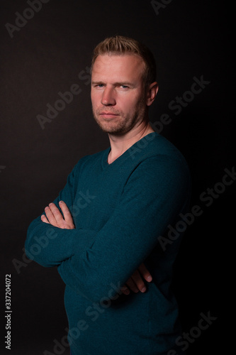 Middle age serious man standing half-sides with arm crossed. Black background
