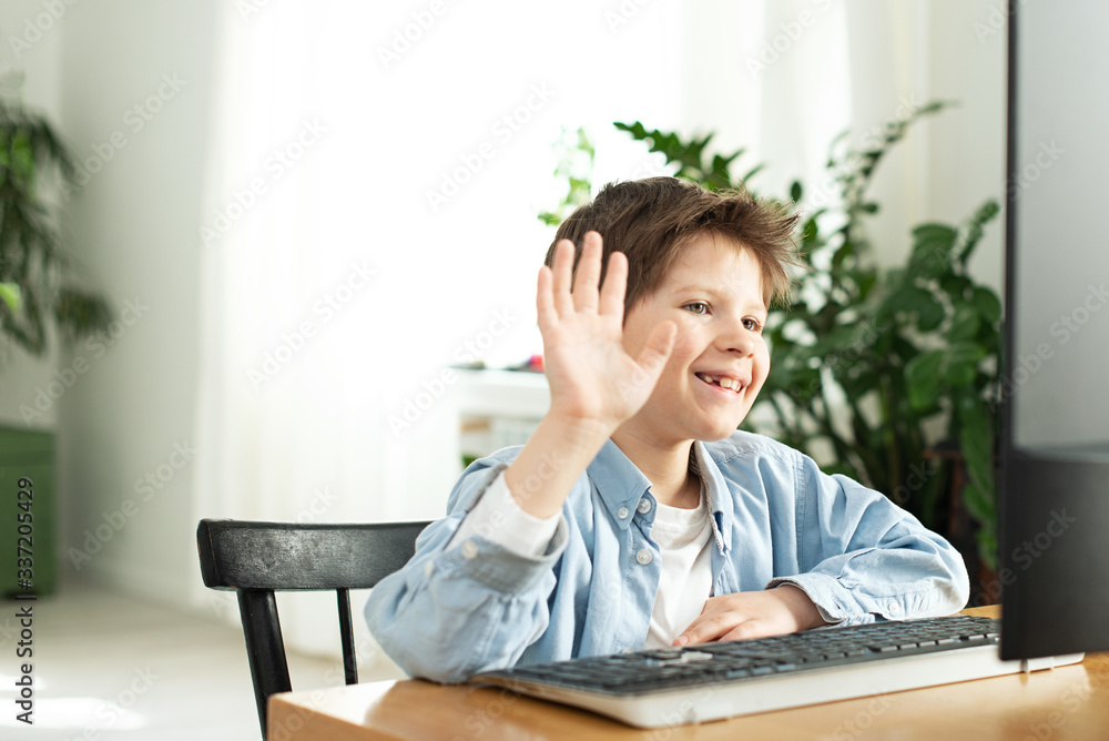 Smiling boy chatting online and waving at the computer screen. Kids and gadgets. Distance learning during isolation during quarantine in coronavirus. Boy and laptop at home. Lifestyle Smiling boy chatting online and waving at the computer screen. Kids and gadgets. Distance learning during isolation during quarantine in coronavirus. Boy and laptop at home. Lifestyle