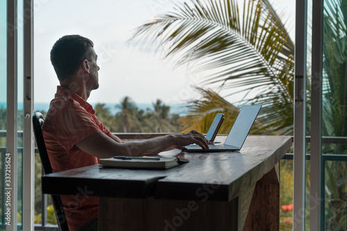 Man works at home at a wooden table with a laptop and smartphone